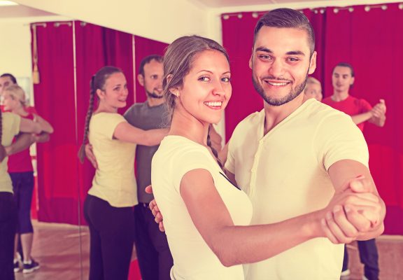 Smiling young men and women enjoying of partner dance in class